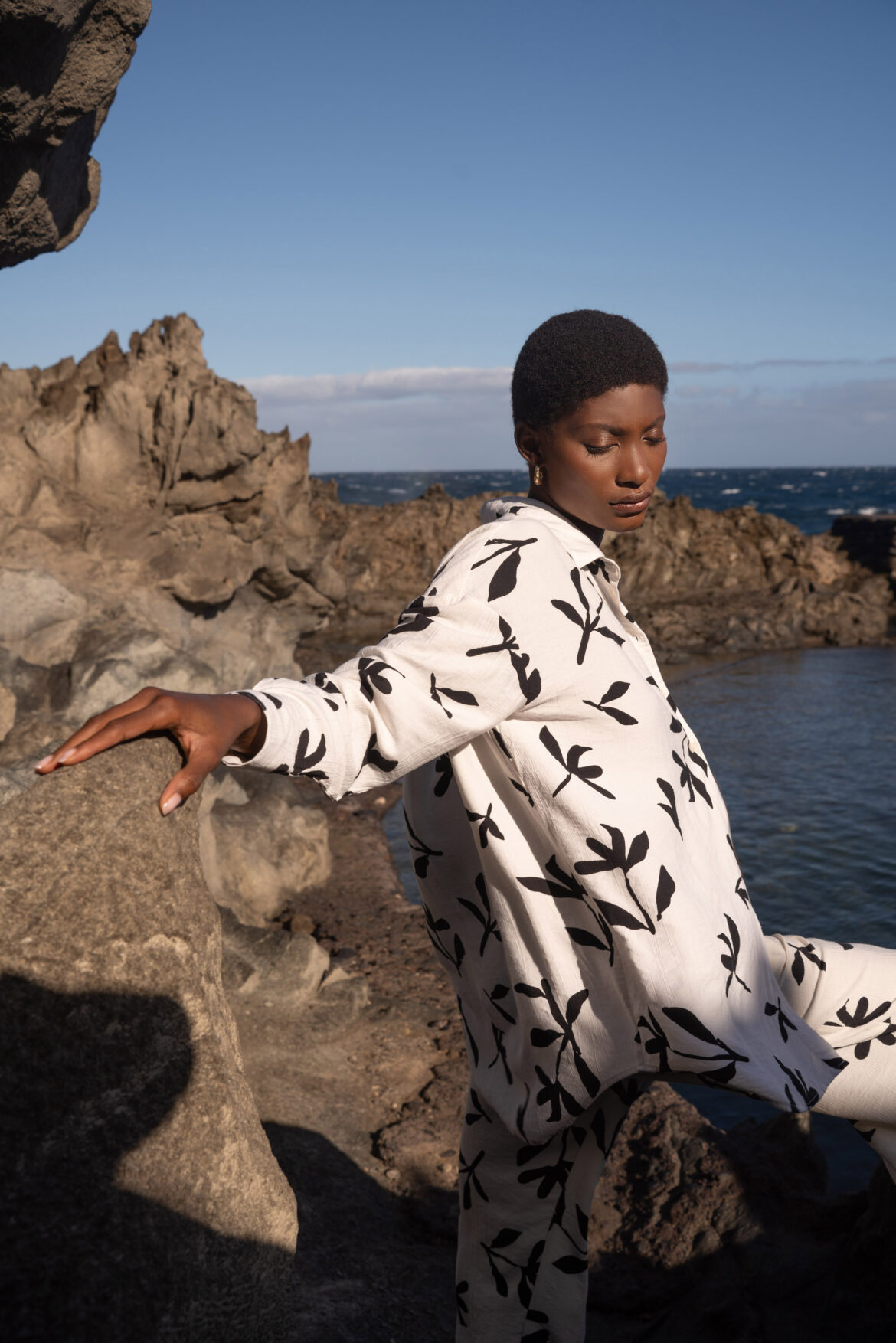 Fashion Photographer London Fashion photography by Pedro Antunes of a model in a white, botanic print outfit by ocean cliffs under blue sky, editorial style. UK fashion photographer. Best fashion photographers in London for brand campaigns and E-commerce